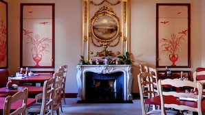 A dining area with red tables and chairs, a fireplace, and decorative mirrors.