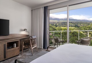 A hotel room with a bed, a desk with a television, and a view of a mountainous landscape.