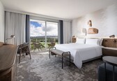 A hotel room with a large bed, a desk, a chair, and a balcony with a view.