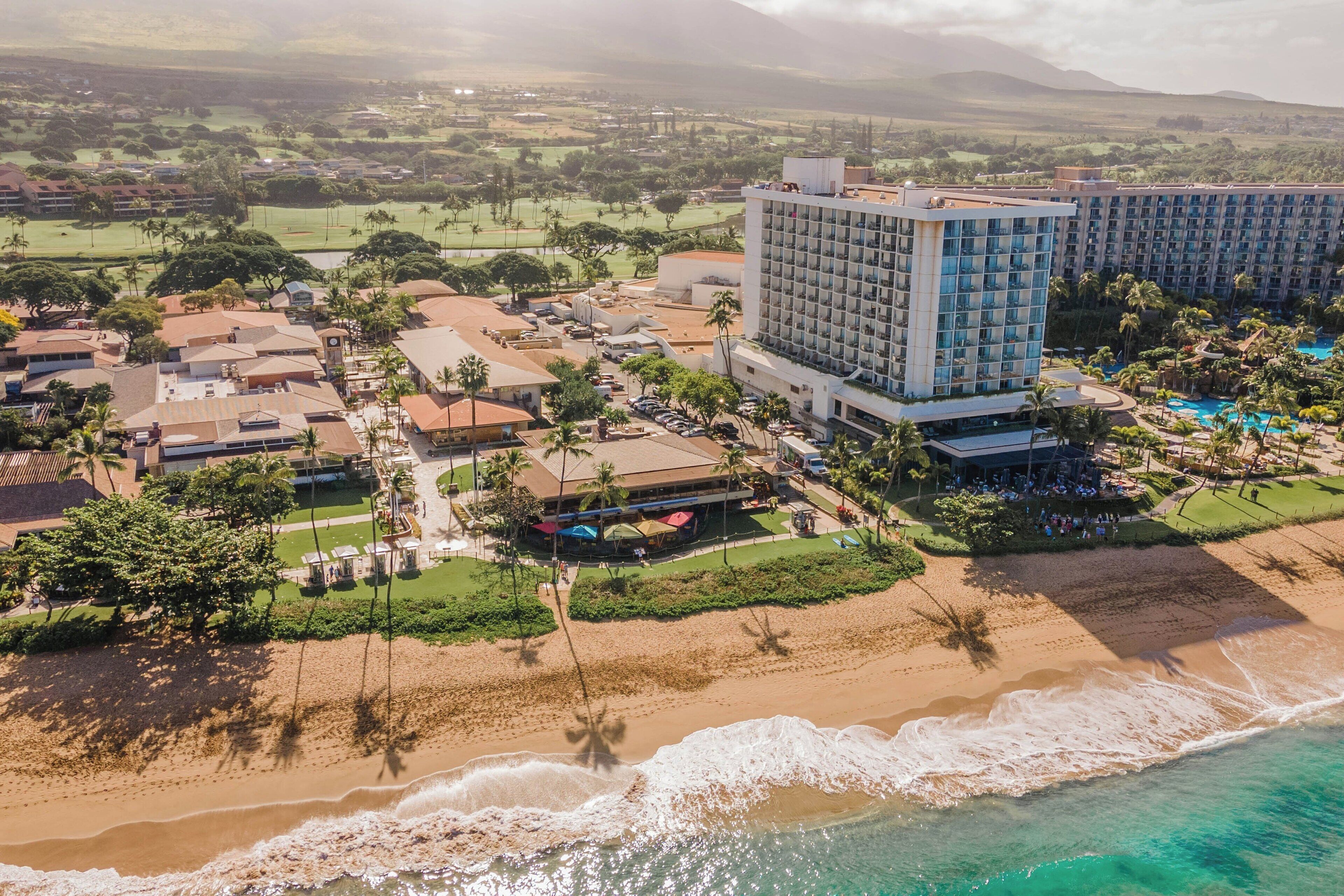 Vista aérea de um resort costeiro com um hotel grande, praia e campo de golfe.