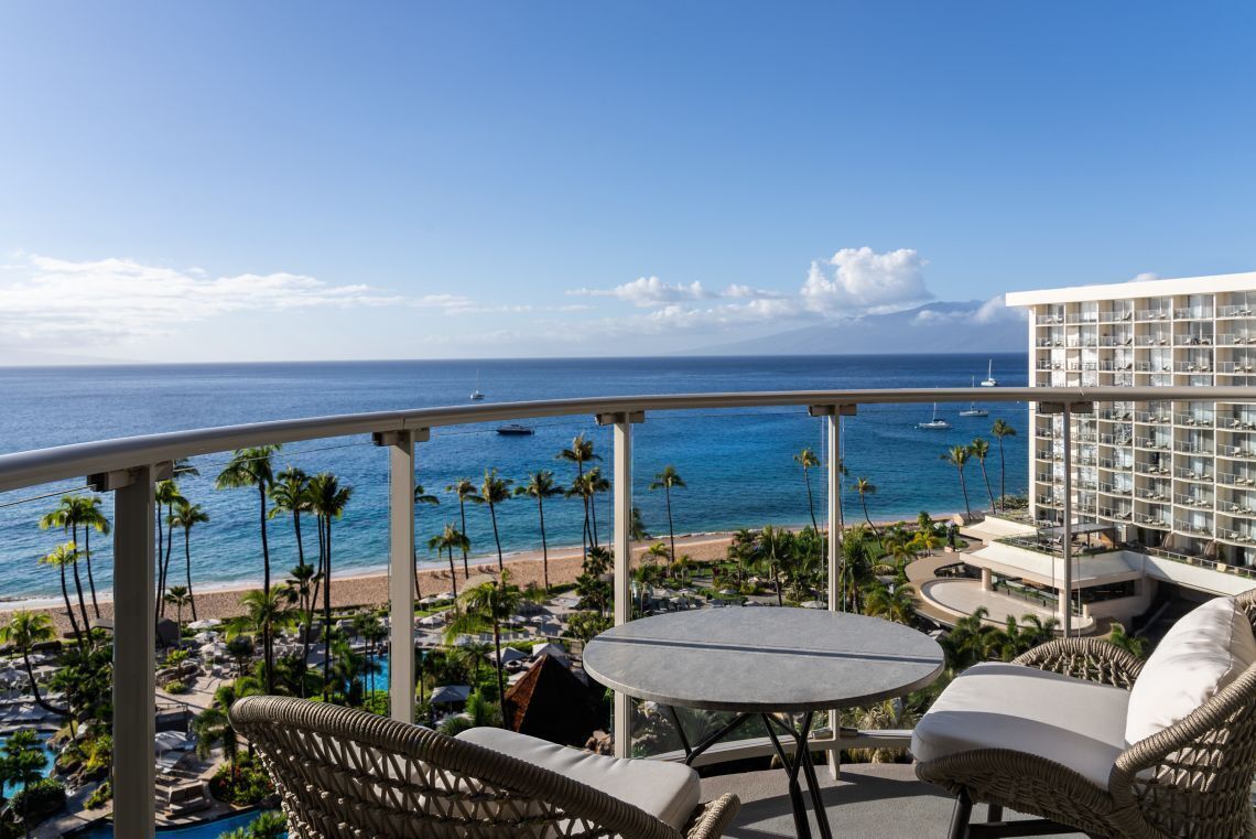 A balcony with a view of the ocean, a pool area, and a building with multiple floors.