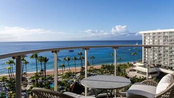 A balcony with a view of the ocean, a pool area, and a building with multiple floors.