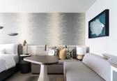 A modern hotel room with a bed, a sofa, a small table, and a wall-mounted artwork.