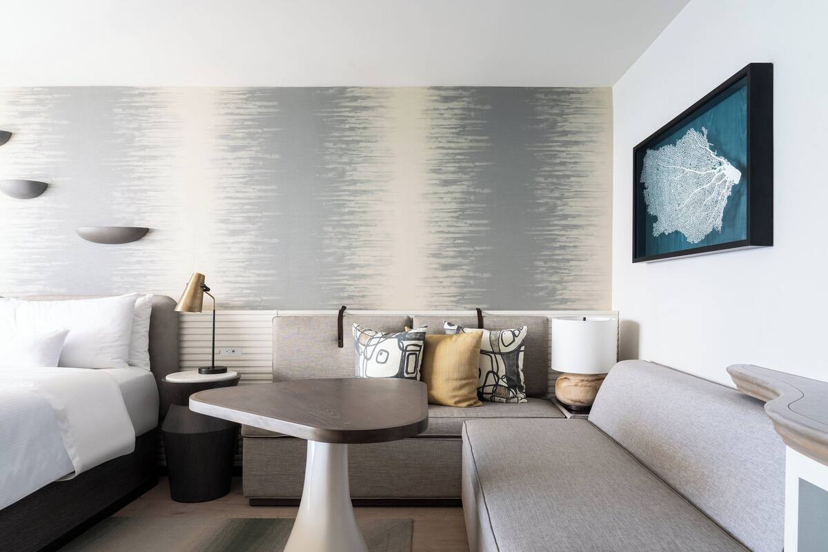 Una habitación de hotel moderna con una cama, un sofá, una mesita y una obra de arte en la pared.