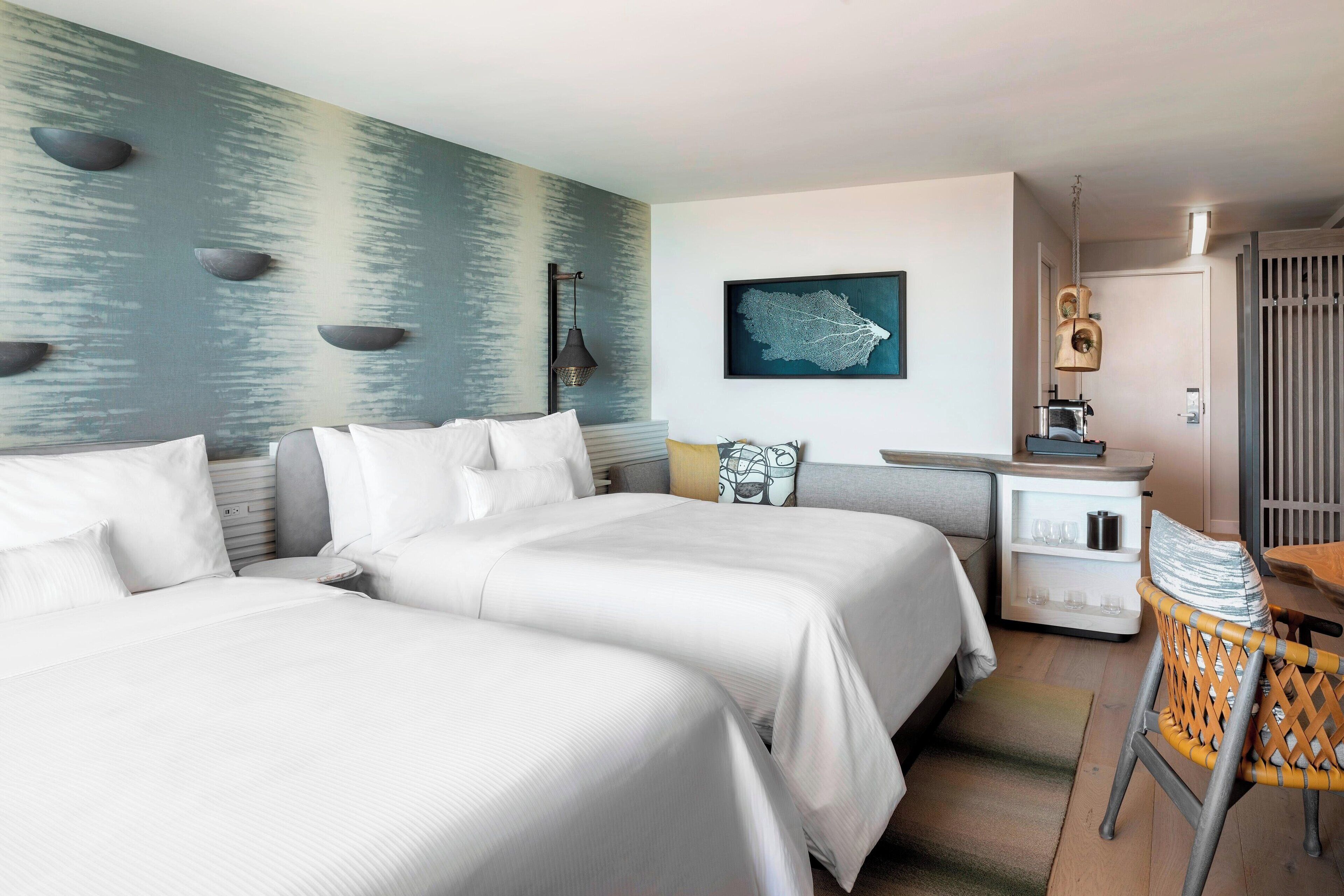 A hotel room with two beds, a desk, a chair, and a wall with a textured design.