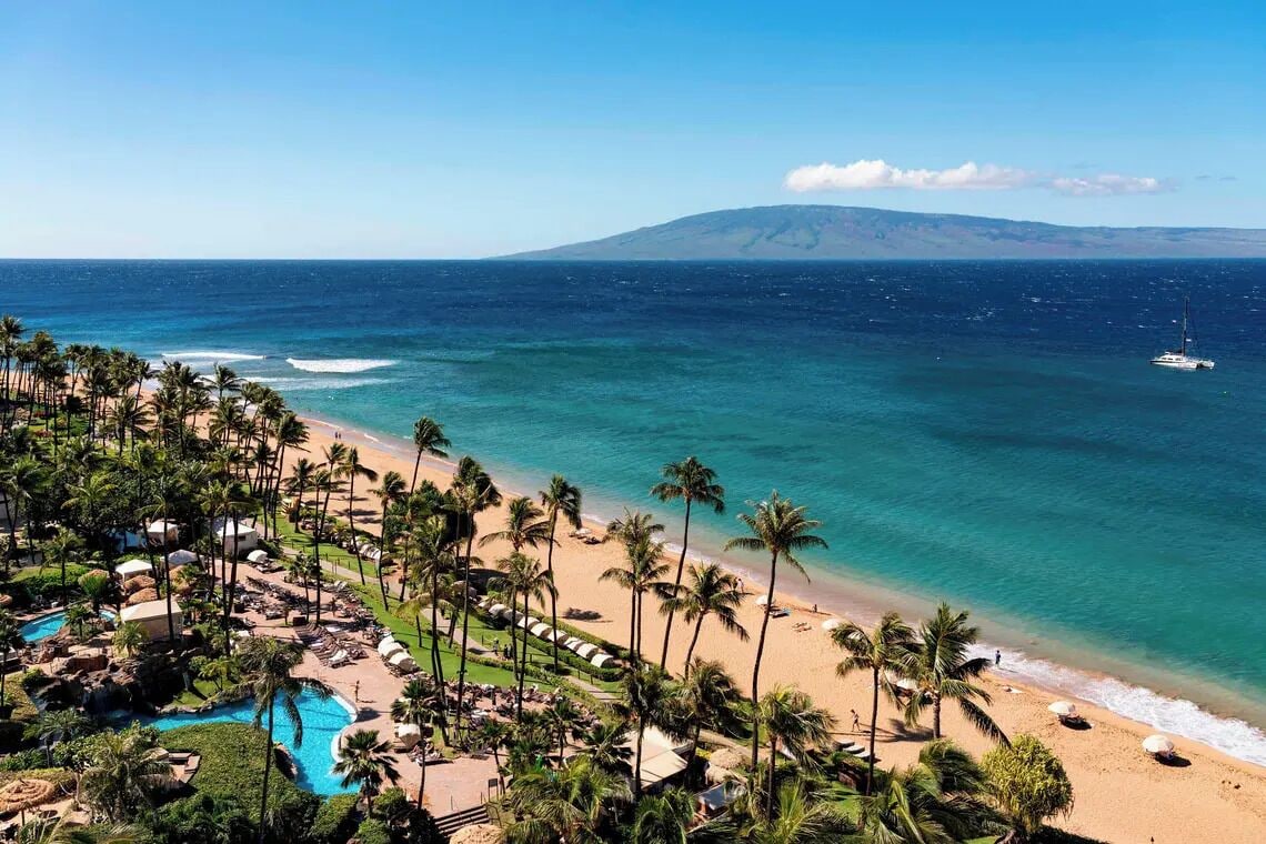 A resort with a beach, palm trees, and a mountain in the background.