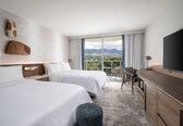 A hotel room with two beds, a desk, a television, and a view of mountains.