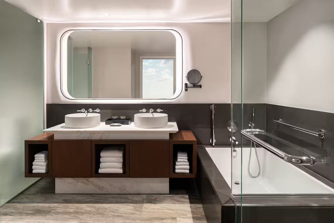 Une salle de bain moderne avec deux lavabos, un grand miroir et une douche à parois de verre.
