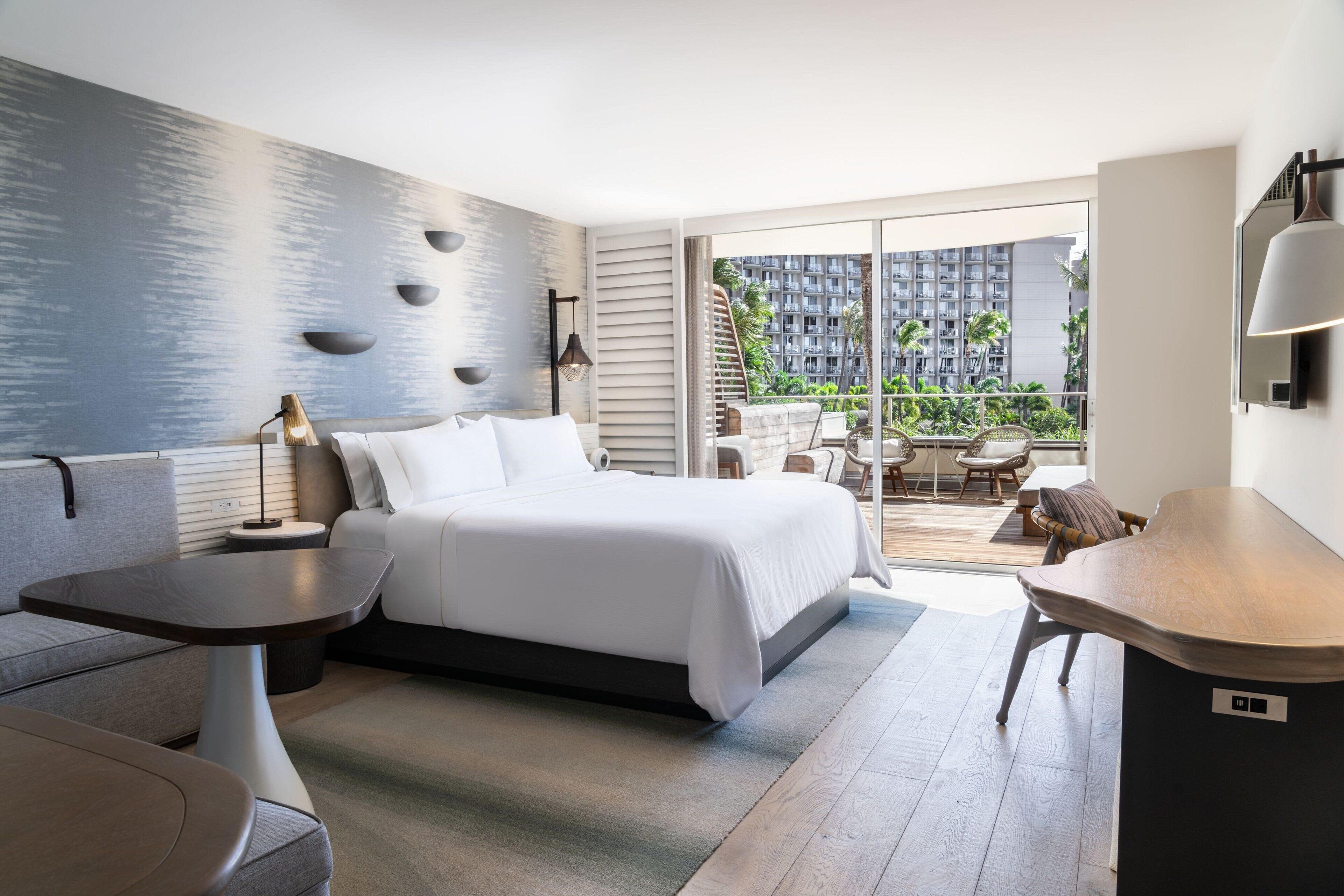 Ein modernes Hotelzimmer mit Bett, einem kleinen Tisch, einer Couch und einem Balkon mit Gartenmöbeln.