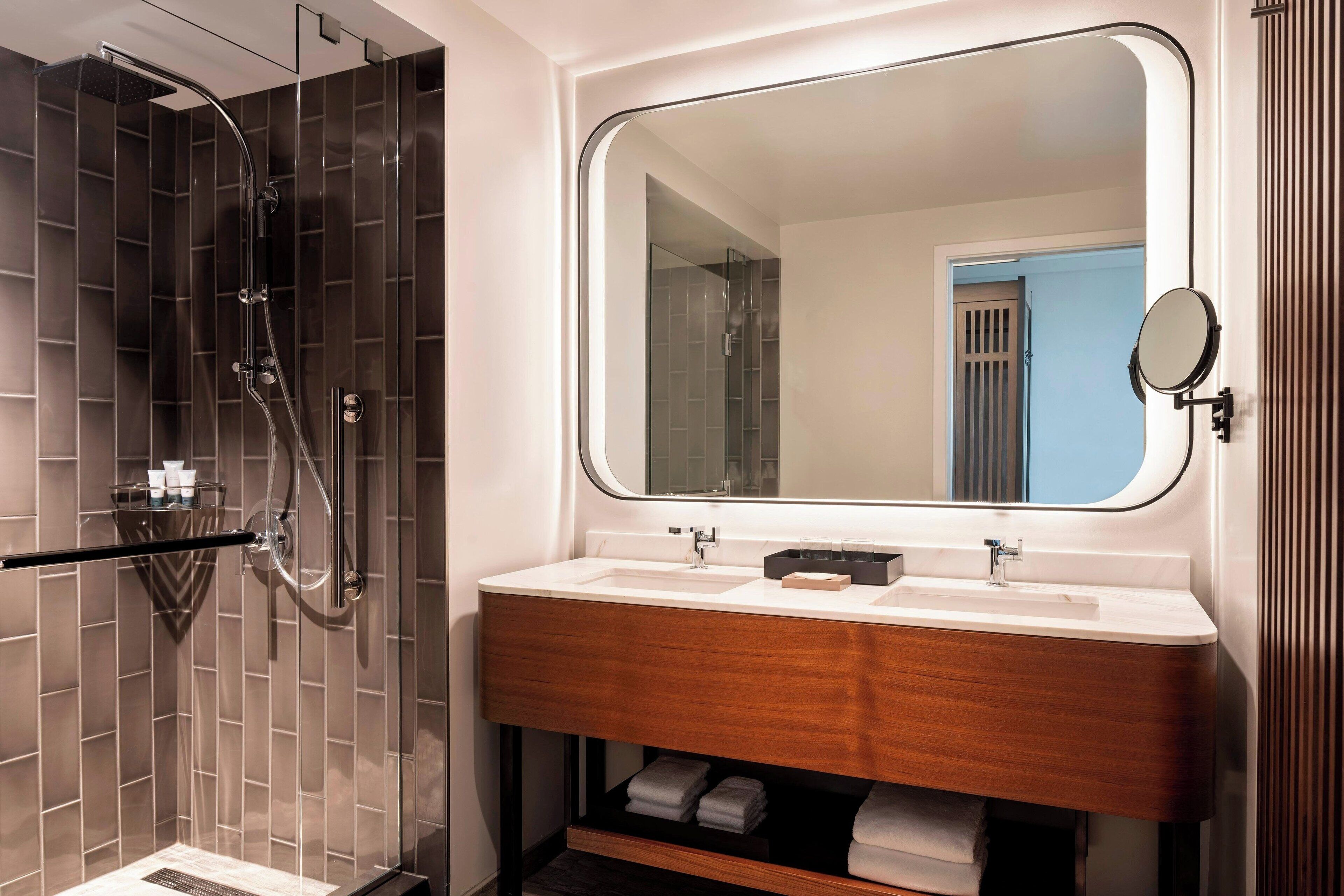 A modern bathroom with a glass-enclosed shower, a large mirror, and a wooden vanity with a sink.