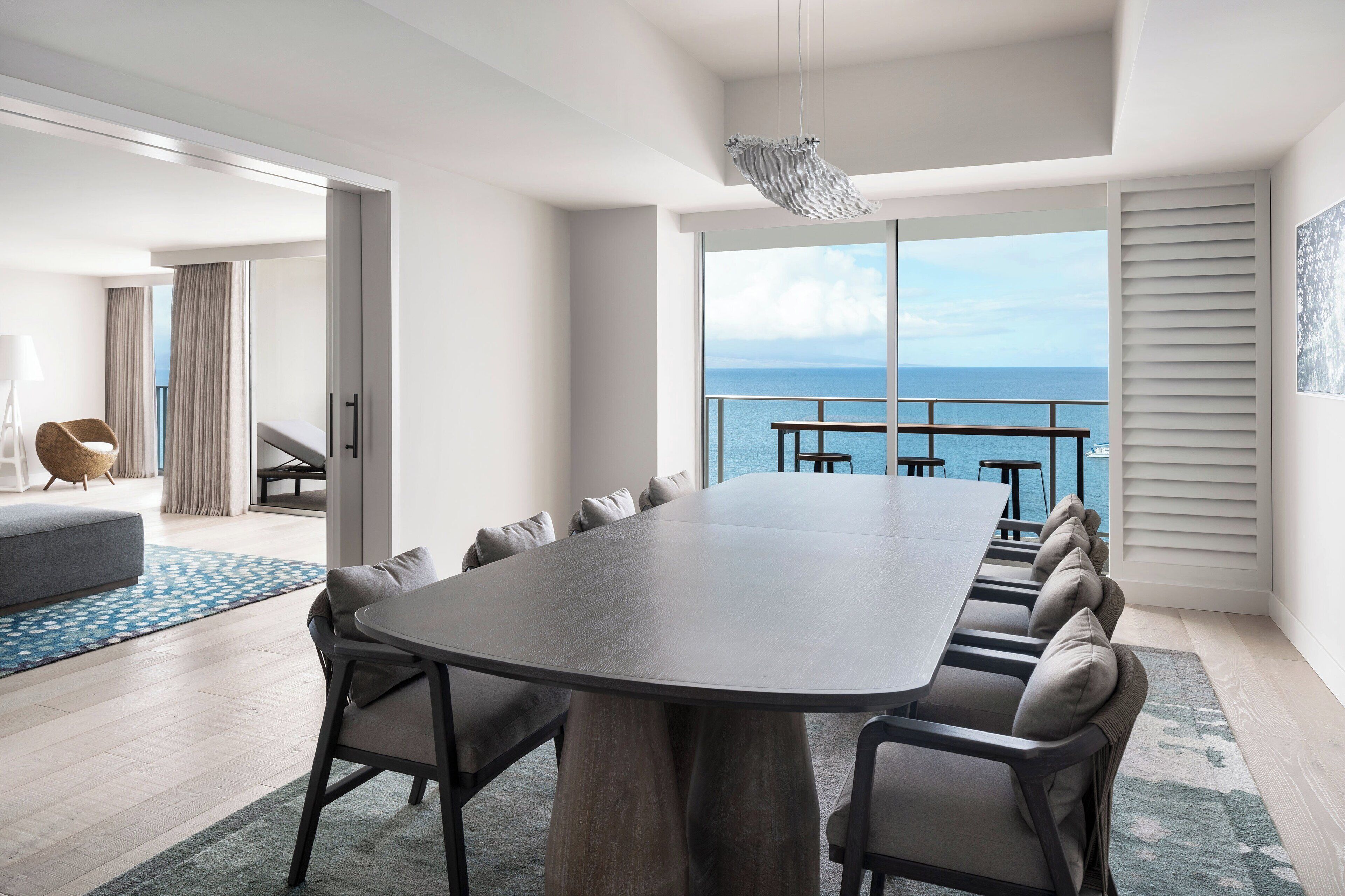 A modern dining area with a large table, comfortable seating, and a view of the ocean.
