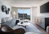 A modern living room with a grey sofa, a round coffee table, wicker chairs, a cabinet, and a large TV on the wall.