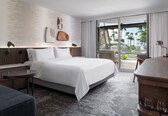 A modern hotel room with a large bed, a small table, a seating area, and a view of the beach.