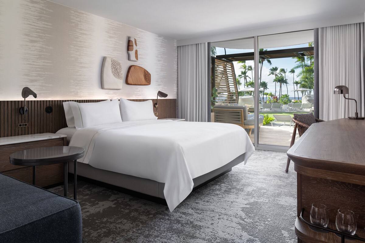 Habitación de hotel moderna con una cama grande, una mesita pequeña, una zona de estar y vista a la playa.