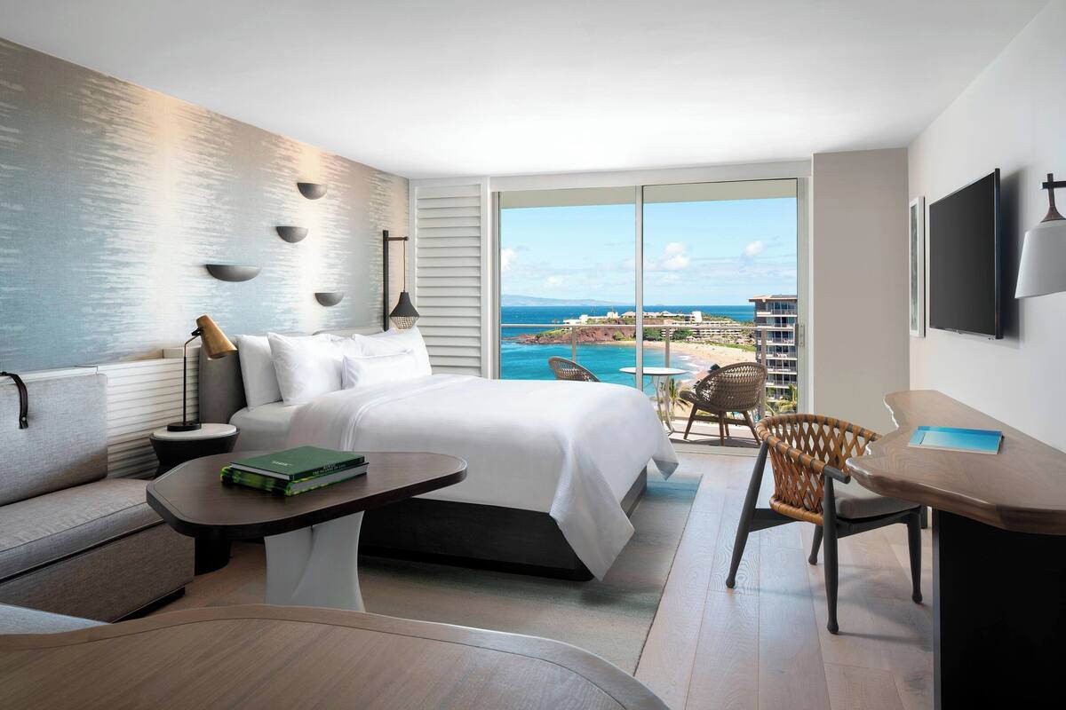 Una habitación de hotel moderna con una cama grande, un sofá, una mesa de comedor y vistas al océano.