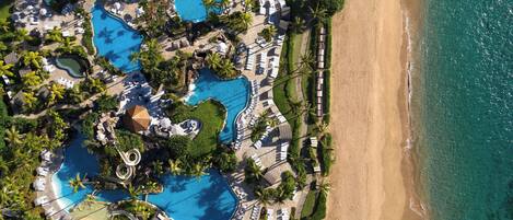 Vista aérea de un resort con varias piscinas, tumbonas y una playa.