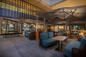 A spacious indoor seating area with blue sofas, wooden tables, and umbrellas providing shade.