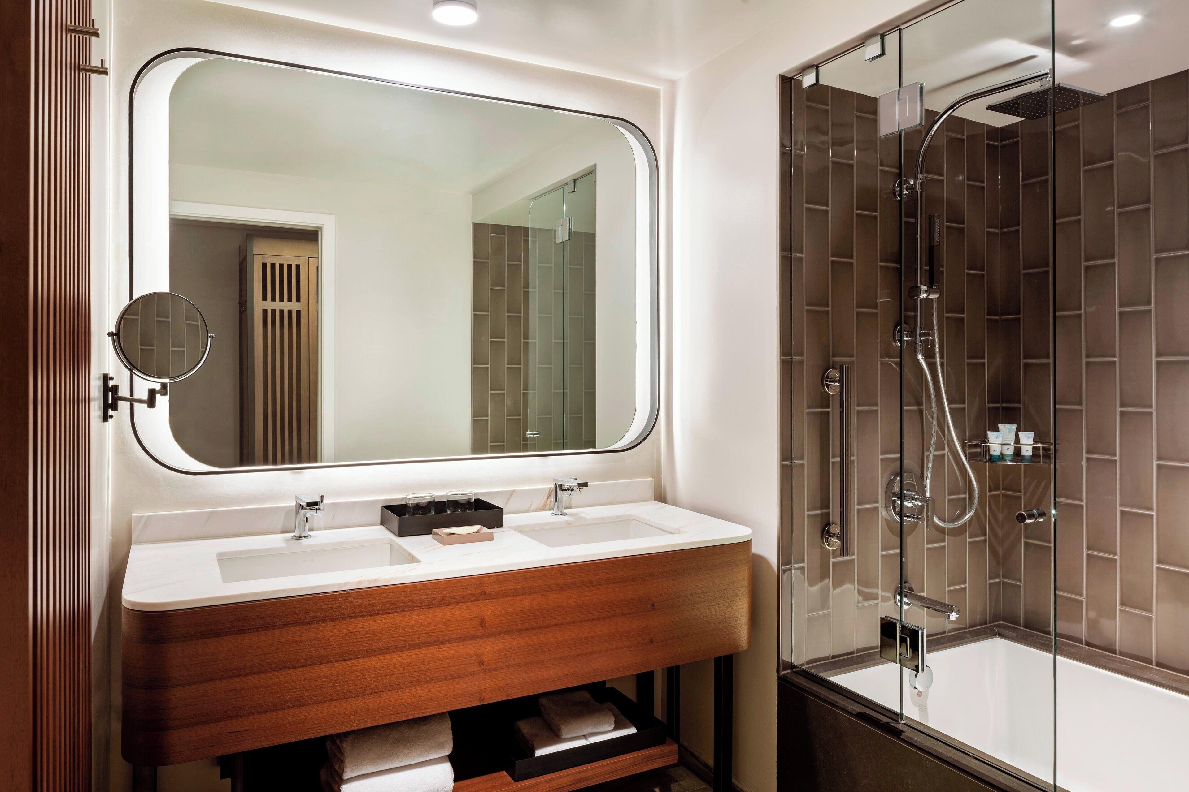Un baño moderno con un espejo grande, dos lavamanos y una ducha con mampara de vidrio.