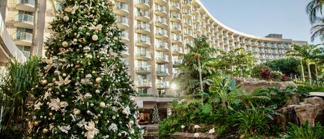Uma grande árvore de Natal decorada em frente a um hotel com fachada curva e várias sacadas.