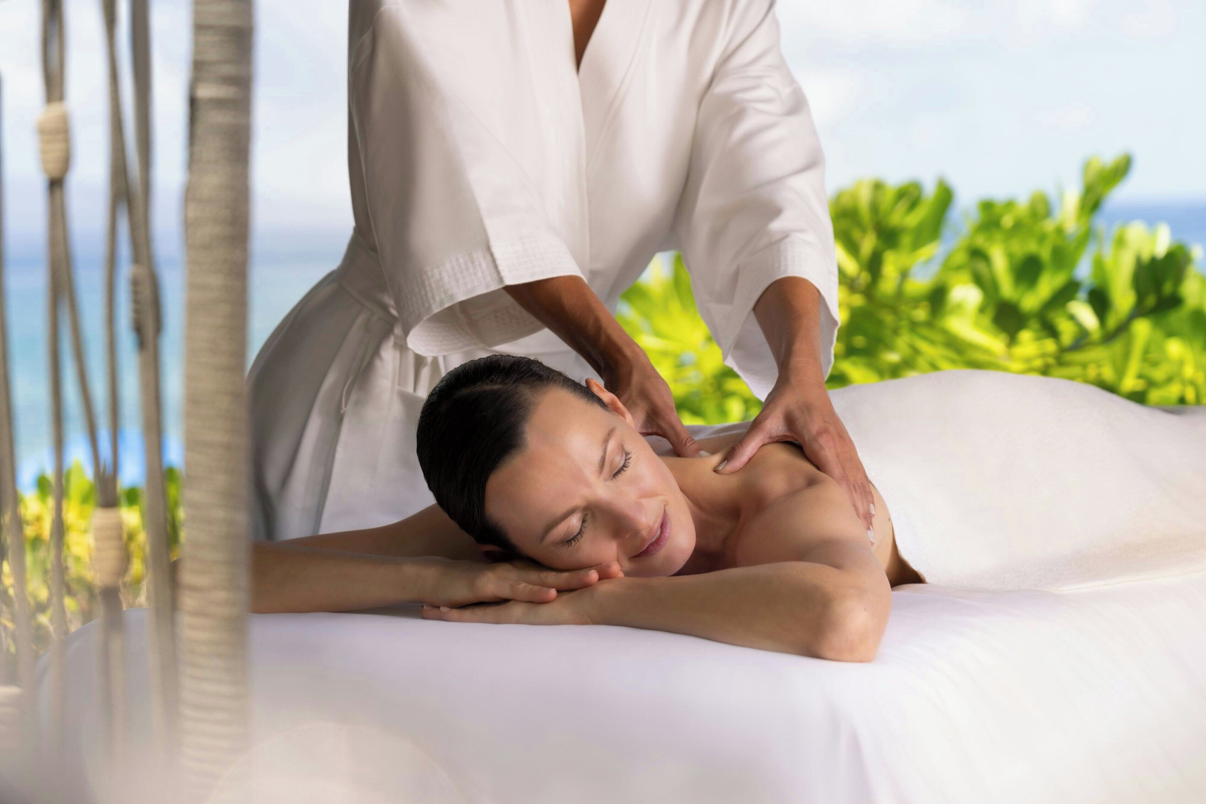 A person receiving a massage in a room with a view of greenery and the sea.