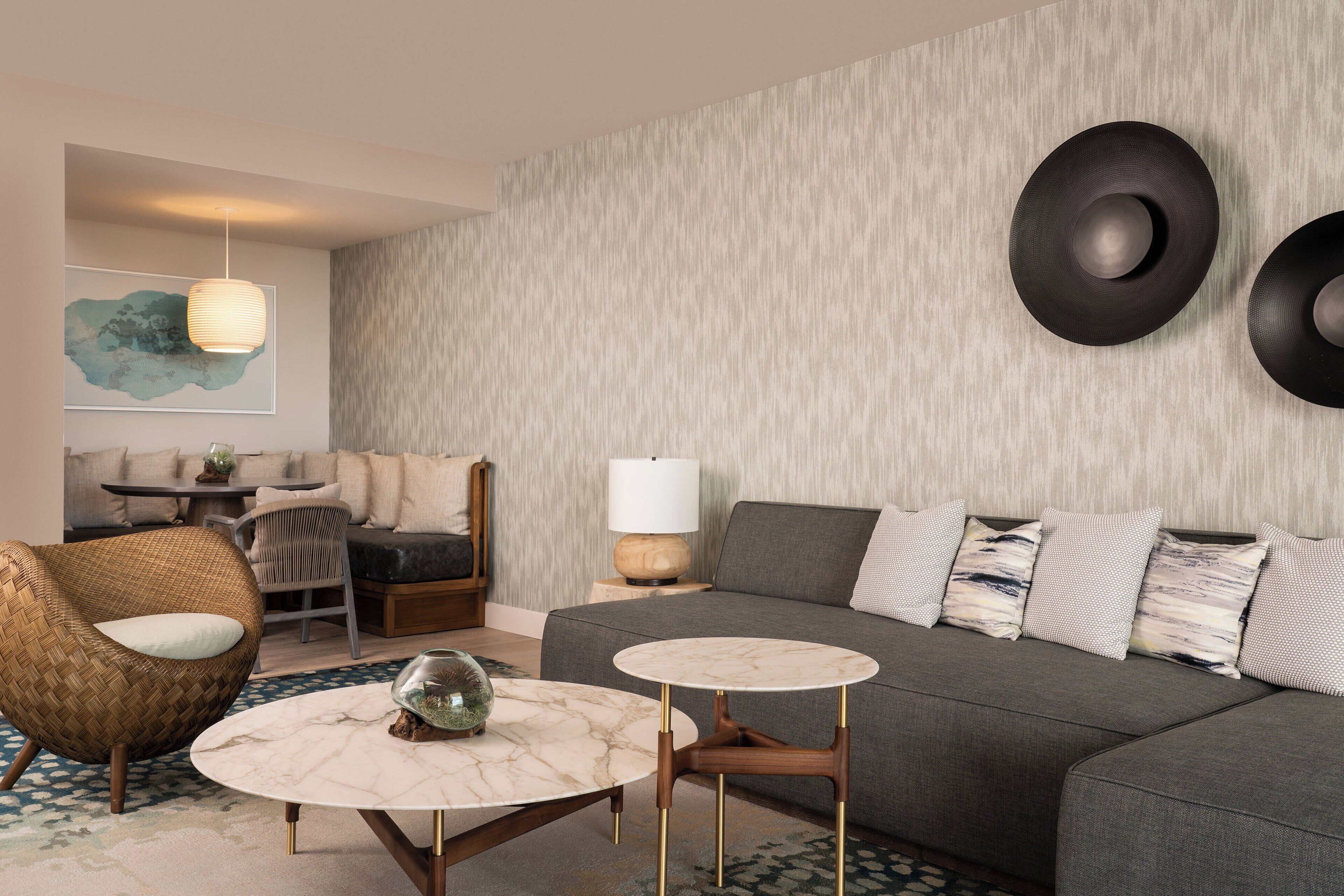 Ein modernes Wohnzimmer mit grauem Sofa, rundem Couchtisch, Korbsessel und einer Wandlampe.