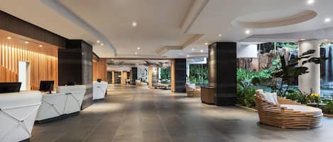 A spacious lobby with a reception desk, seating area, and a view of a waterfall.