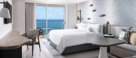 Une chambre d’hôtel moderne avec un grand lit, une table à manger, une chaise et une vue sur l’océan.
