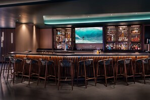 A bar area with a large screen displaying a surfer, bar stools, and shelves stocked with bottles.
