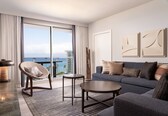 A modern living room with a sofa, a chair, a coffee table, and a view of the ocean through large windows.