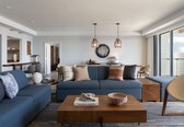 A modern living room with a blue sofa, wooden coffee table, and hanging pendant lights.