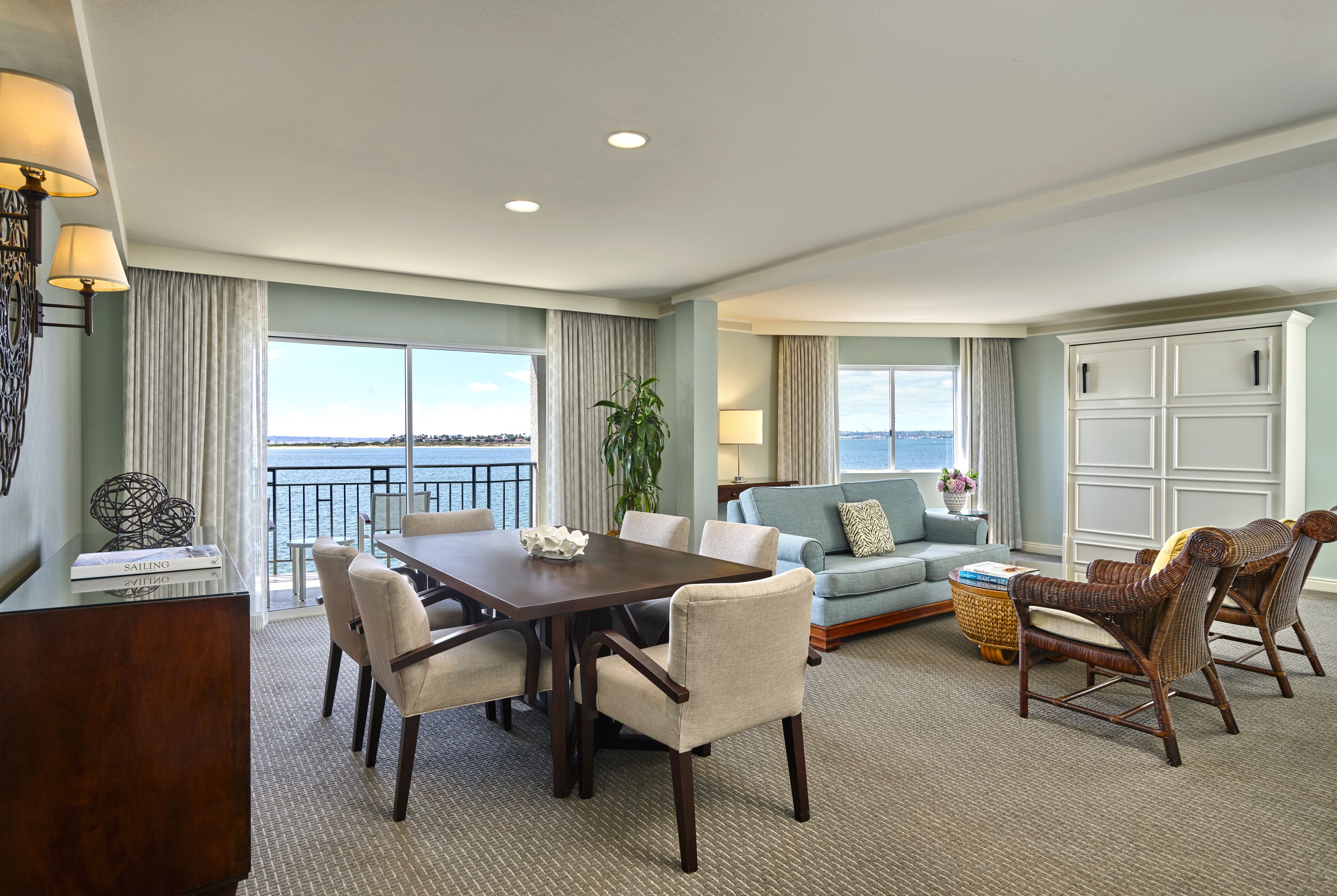 A spacious living room with a dining area, large windows with a view, and a balcony.