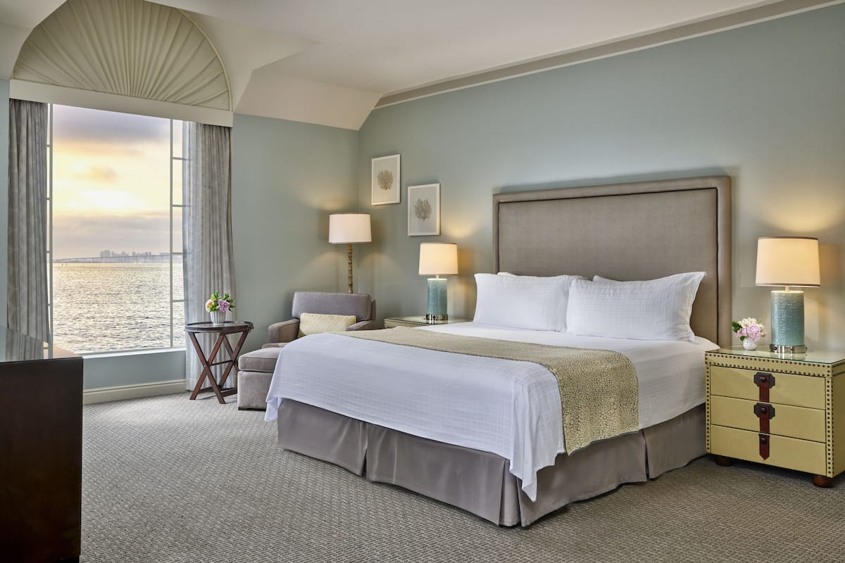 A hotel room with a large bed, two bedside tables, a chair, and a view of the water.