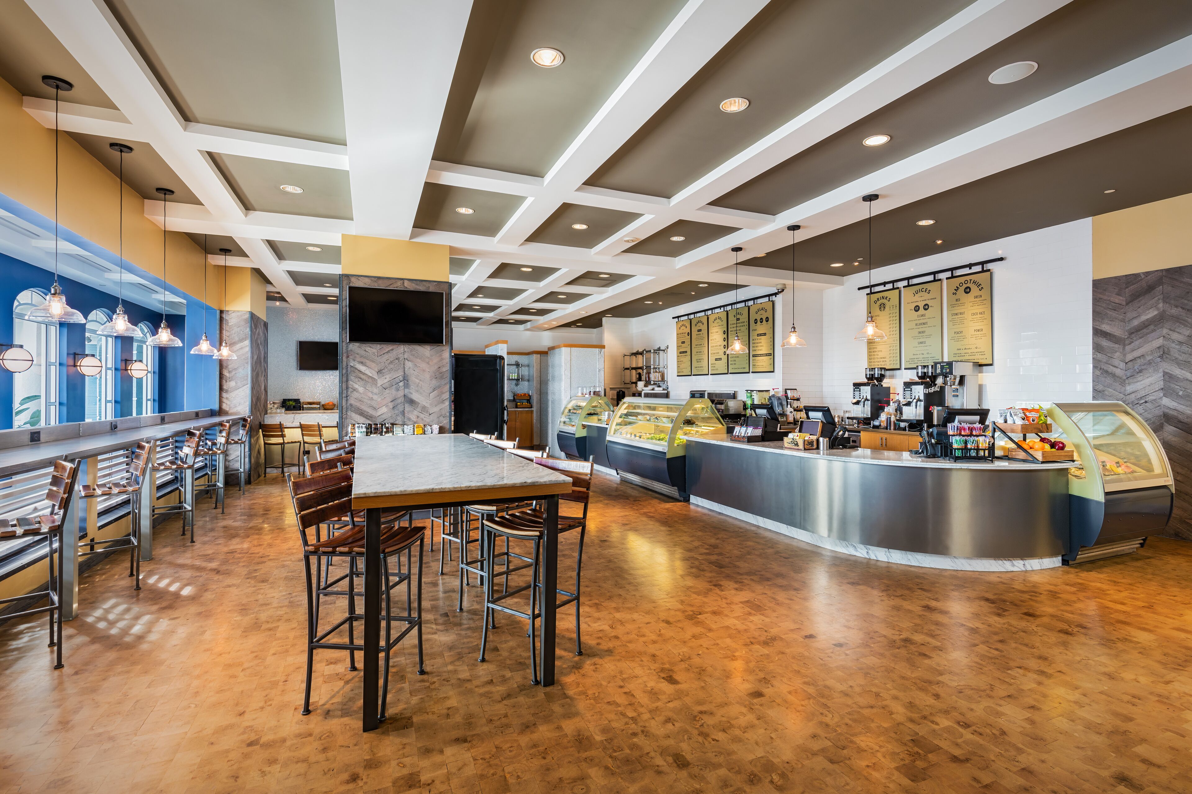 Un restaurante moderno con una barra central, diferentes disposiciones de asientos y un mostrador con productos alimenticios.