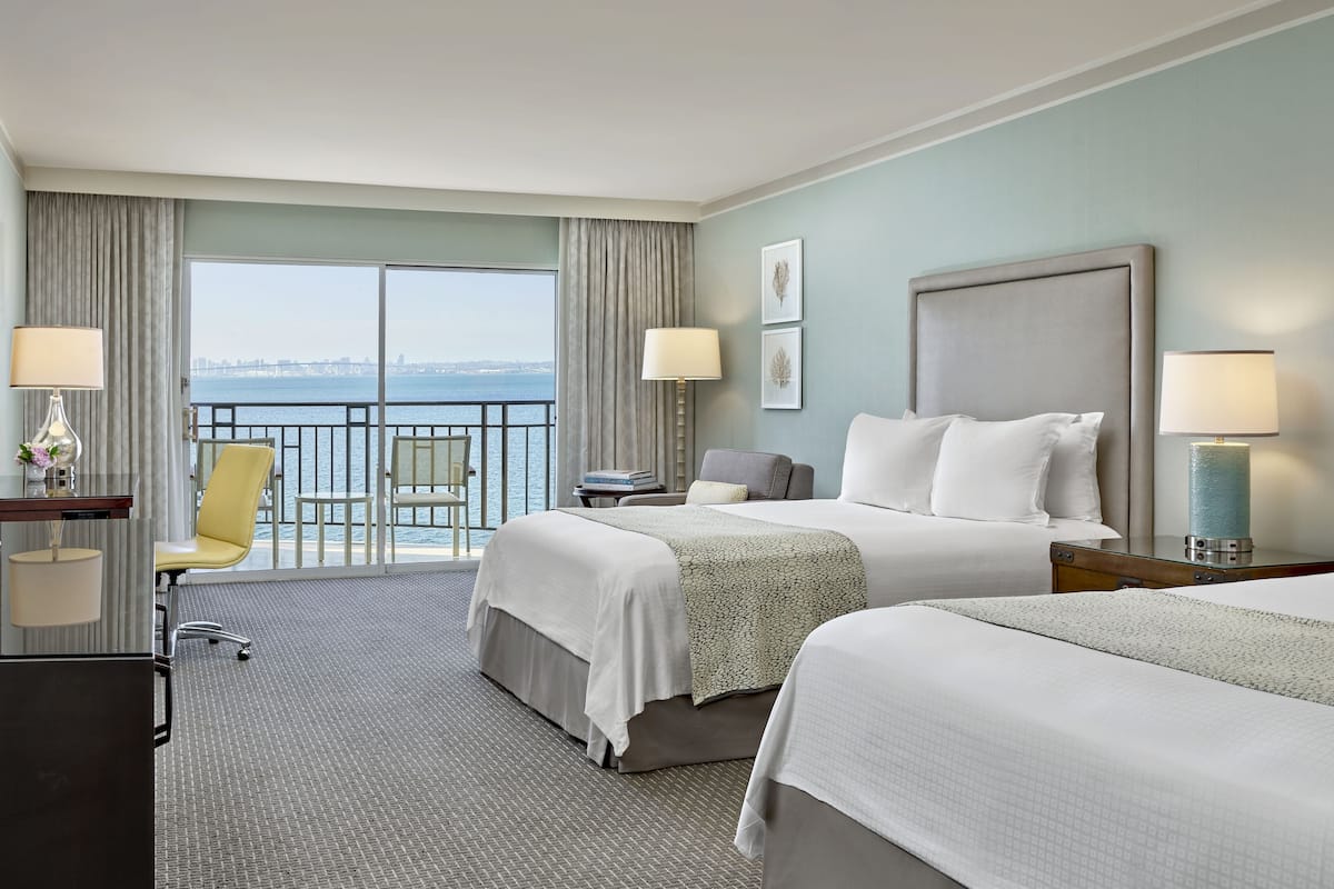 A hotel room with two beds, a desk, a chair, and a view of the water.