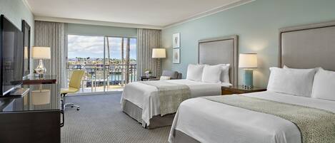A hotel room with two beds, a desk, and a chair. There is a large window with a view of palm trees and buildings.