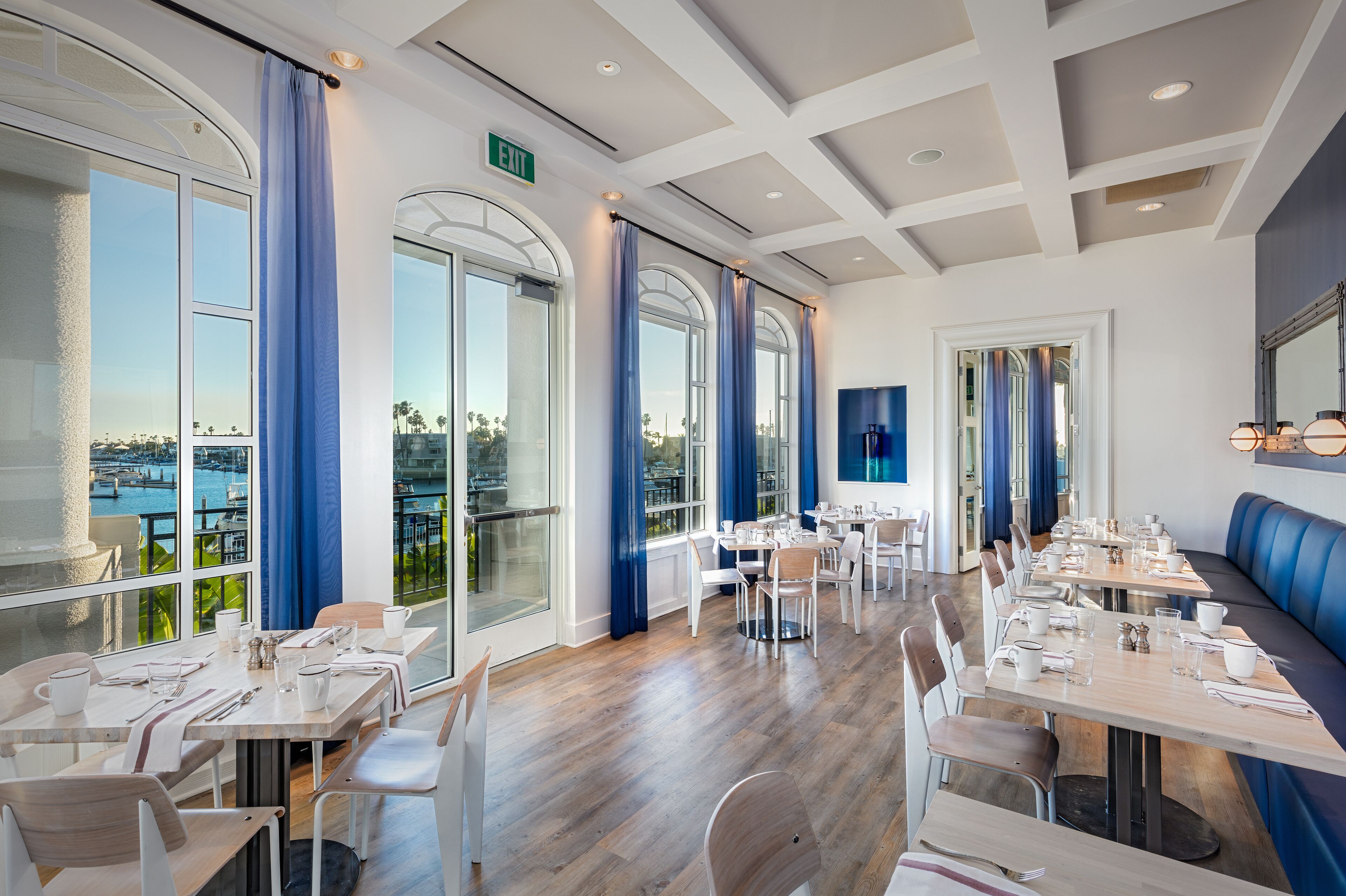 A restaurant with large windows, a long dining table, and a blue cushioned bench.