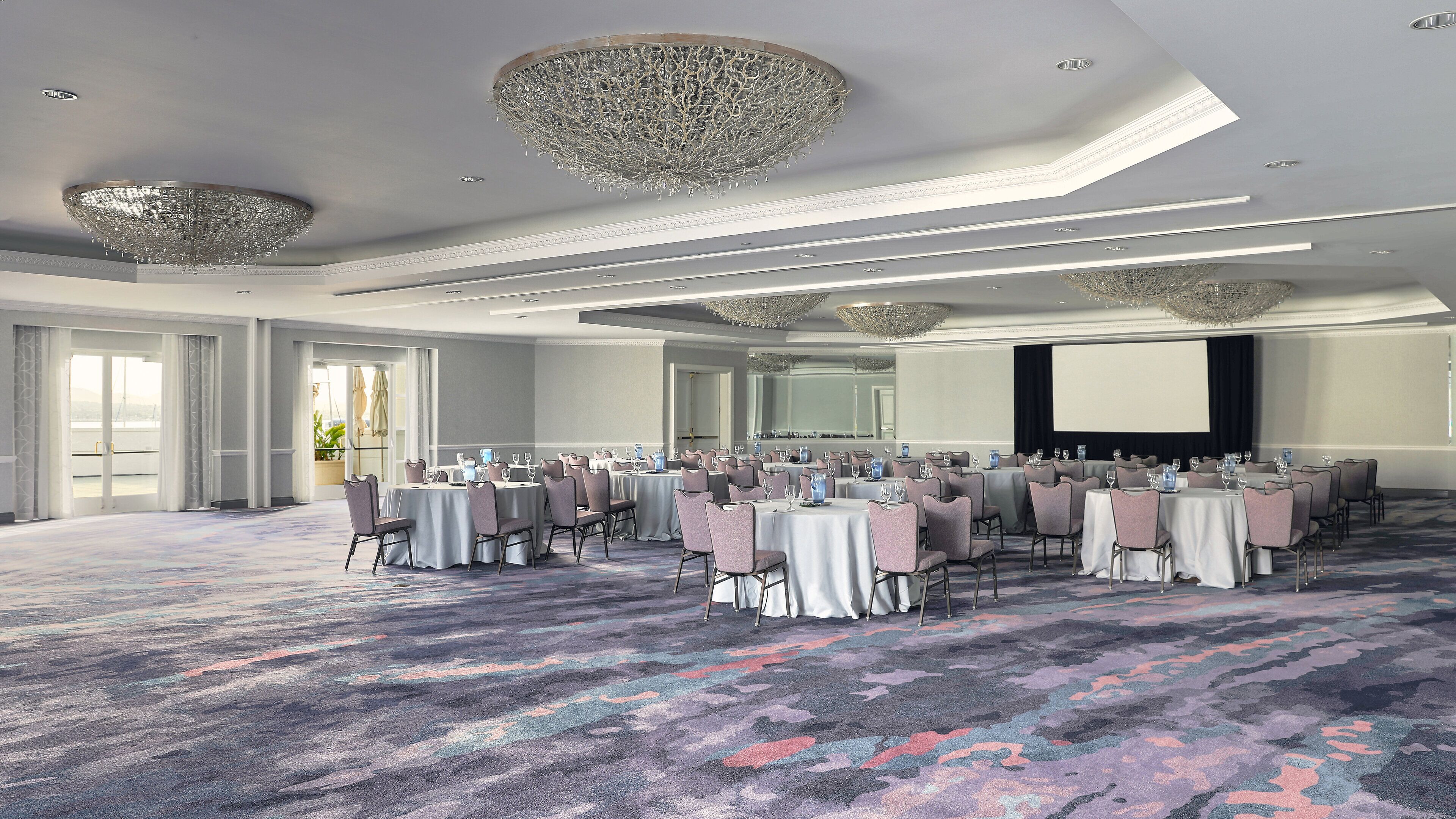 A conference room with round tables, chairs, and a large screen.