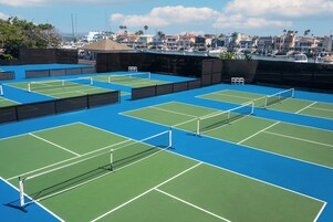 A tennis court complex with multiple courts, a net, and a backdrop of residential buildings.
