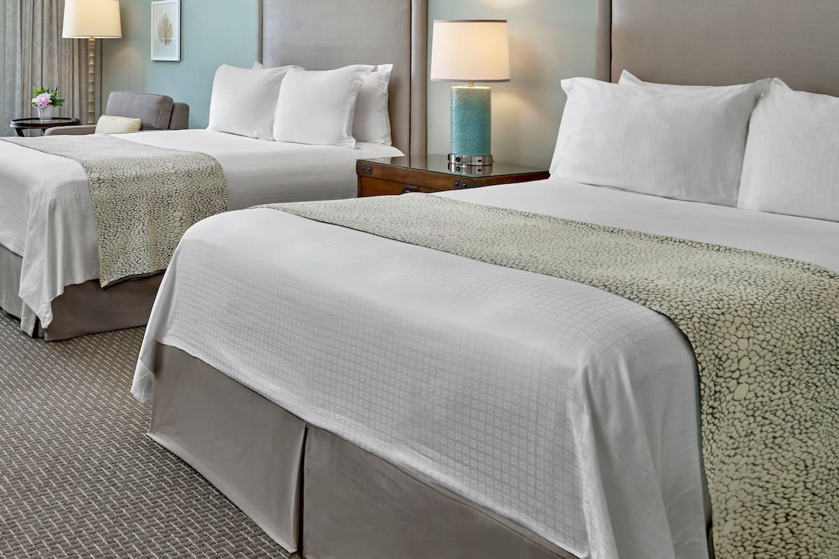A hotel room with two beds, each with a headboard, a nightstand with a lamp, and a small table with a vase of flowers.