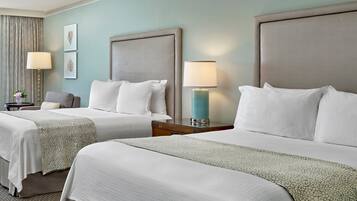A hotel room with two beds, each with a headboard, a nightstand with a lamp, and a small table with a vase of flowers.