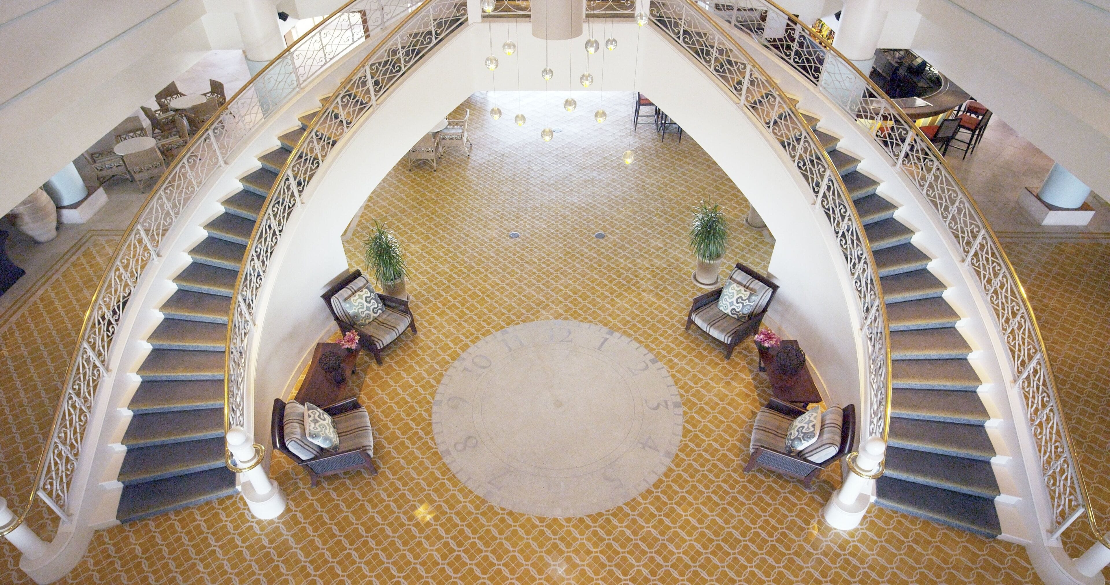 A grand lobby with a central circular area, a staircase with ornate railings, and seating arrangements.