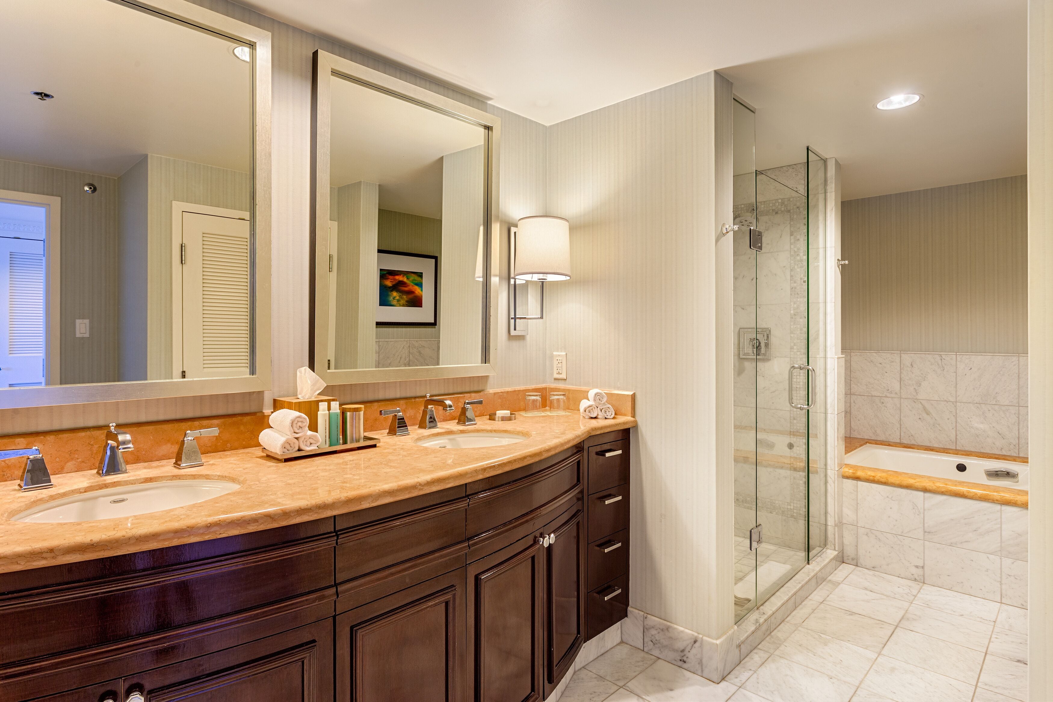 A modern bathroom with two sinks, a large mirror, a glass-enclosed shower, and a bathtub.