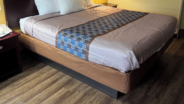 A hotel room with a large bed, a bedside table with a phone, and a lamp. - Somatel Goodlettsville (Goodlettsville)
