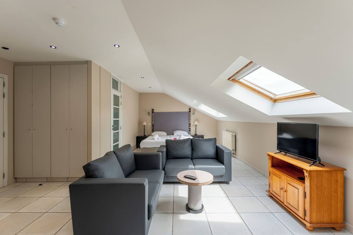 A modern living room with a sofa, a coffee table, a TV on a wooden stand, and a skylight above.