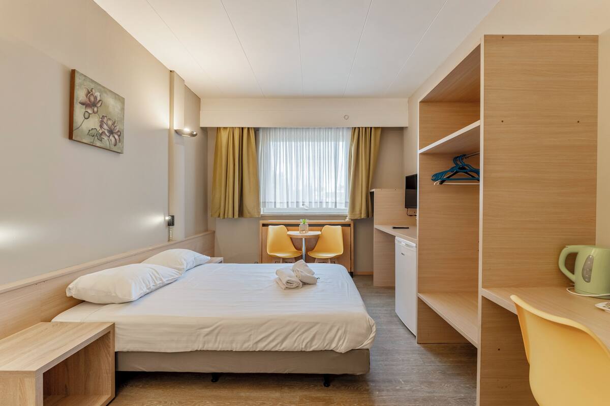 A hotel room with a bed, a desk, a chair, a TV, and a wardrobe.