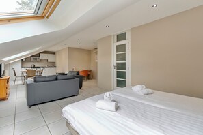 A modern hotel room with a skylight, a sofa, a bed, and a kitchenette in the background.