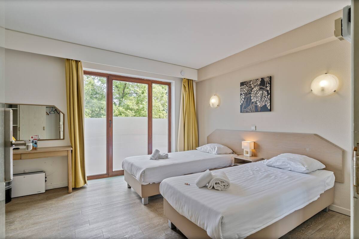 A hotel room with two beds, a desk, a mirror, and a window with curtains.