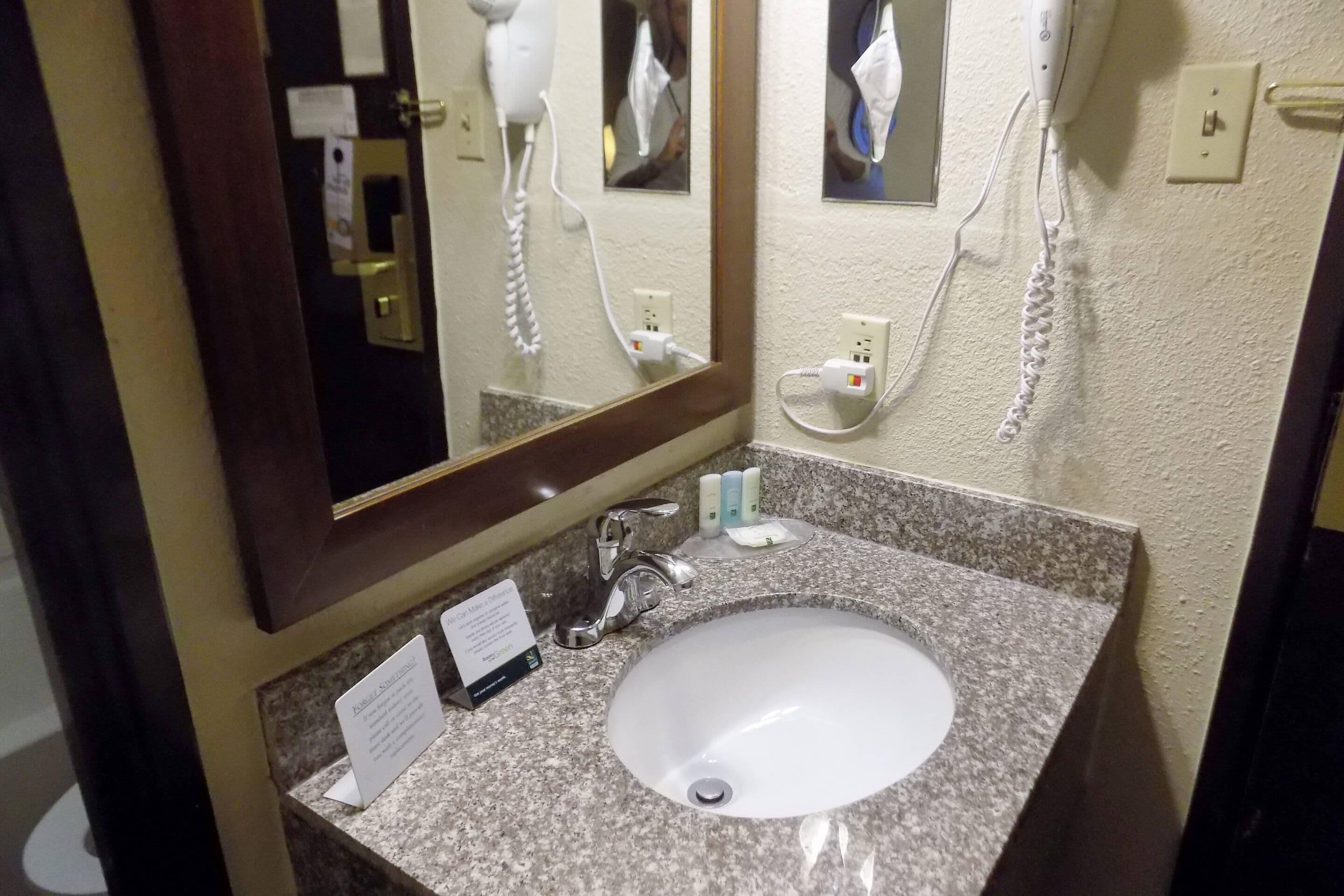 A bathroom with a granite countertop, a white sink, a mirror, a hairdryer, and a phone.
