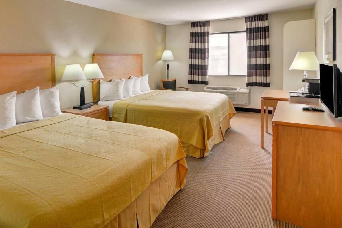 A hotel room with two beds, a desk, a television, and a window with curtains.