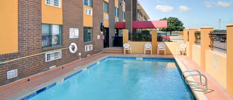 A swimming pool with a 5 ft no diving sign, surrounded by a brick building with multiple windows and a red awning.